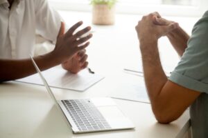 Two men in a meeting with a laptop and documents on the table.